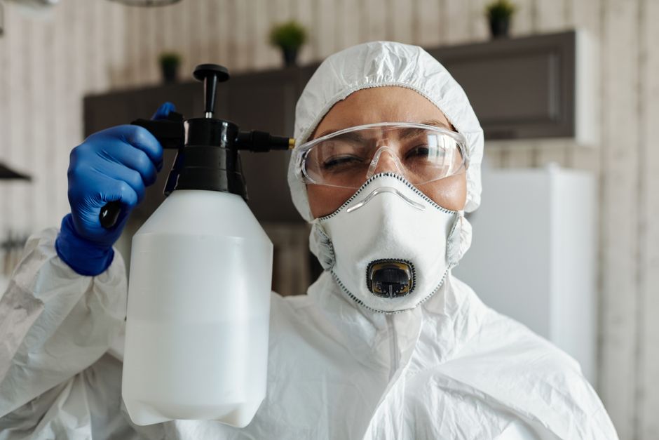 Female wearing protective equipment and spraying disinfectant indoors.