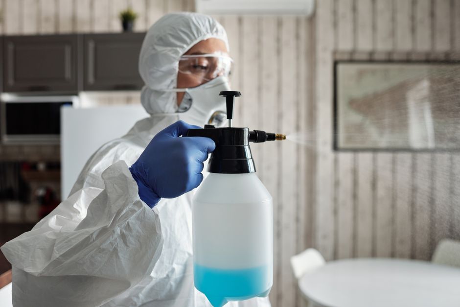 Professional in full gear disinfecting indoor area using a spray bottle for COVID-19 prevention.